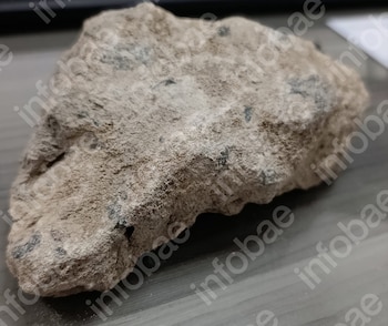 Una piedra grande de textura rugosa y superficie irregular permanece apoyada sobre una mesa plana