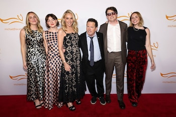 Michael J. Fox, Tracy Pollan y sus hijos posan sonrientes en una alfombra roja, con un fondo blanco que muestra el logo naranja de la fundación