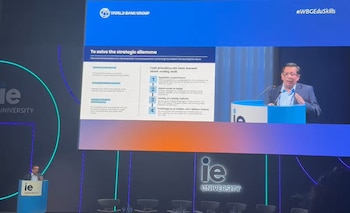 Hombre en podio habla frente a pantalla con presentación que muestra el logo del Banco Mundial, texto y gráficos. Logos IE University visibles
