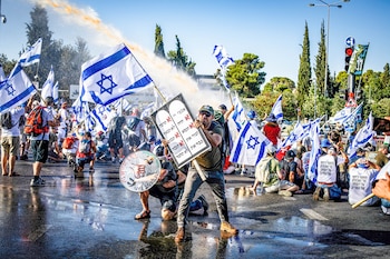 Manifestantes se cubren cuando un cañón de agua de la policía les dispara durante una manifestación contra la reforma judicial frente a la Knesset. (Europa Press/Contacto/Eyal Warshavsky)