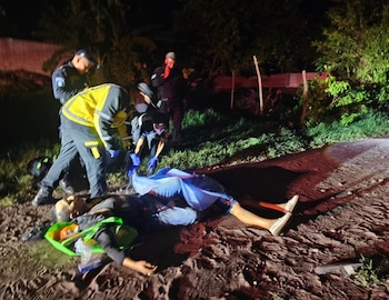 Cuatro personas con uniformes y guantes azules asisten a un individuo acostado en el suelo, parcialmente cubierto por una tela celeste, en una zona oscura con vegetación