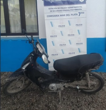 Una motocicleta negra sobre suelo de piedra ante una pancarta oficial de la Comisaría Séptima de Mar del Plata