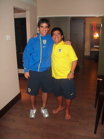 Dos hombres con ropa de Boca Juniors. Uno de azul, shorts y zapatillas. Otro de amarillo, shorts, descalzo. Fondo de interior. Fecha visible 2004