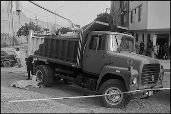 Un camión de carga en blanco y negro estacionado junto a una lona en el suelo y una cinta de seguridad en primer plano.