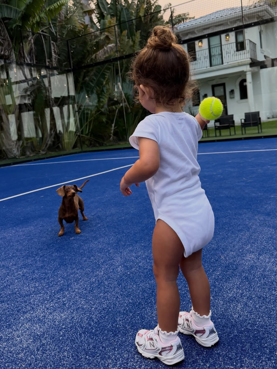 Olivia, en una cancha de tenis, jugando con el perro salchica de la familia