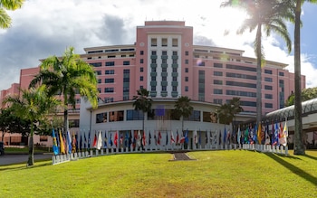 Edificio rosa de múltiples pisos, palmeras, un césped verde, y una hilera de banderas de estados y territorios estadounidenses