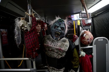 Un personaje con máscara azul de monstruo y pechera dentro de un autobús junto a muñecos colgados y adornos de temática de terror