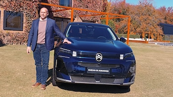 Pablo García Leyenda, sonriente, de pie junto a un SUV Citroën C5 Aircross azul oscuro sobre césped. Detrás, un edificio con enredaderas rojas otoñales y árboles