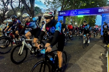 Un grupo de ciclistas con cascos y prendas deportivas avanza en bicicleta debajo de un arco azul del evento Gran Fondo Argentina