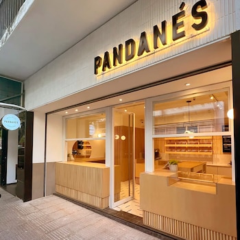 Fachada de un local comercial con un letrero iluminado que dice PANDANÉS, mostradores de madera, puertas de vidrio e iluminación interior