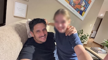 Un hombre y una niña con el rostro difuminado sobre un sillón beige, junto a dos cuadros en la pared y plantas.