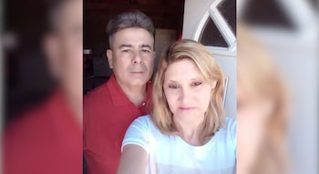 Un hombre con camisa roja y una mujer con cabello rubio posan frente a una puerta blanca