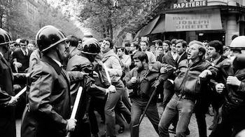 Imagen en blanco y negro de policías con cascos y porras blancas enfrentándose a un grupo de jóvenes manifestantes en una calle urbana de París