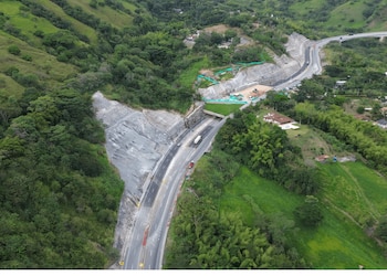 Una vista aérea de una carretera de dos sentidos con un túnel, maquinaria pesada en una zona de excavación y árboles a los lados