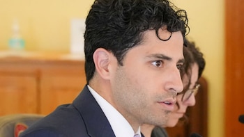 Primer plano de un hombre con cabello rizado oscuro, traje azul y camisa blanca mirando hacia la derecha