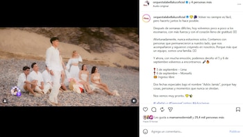 Seis jóvenes, tres hombres y tres mujeres, vestidos de blanco, posan sentados y de pie en una playa rocosa con una duna de arena al fondo