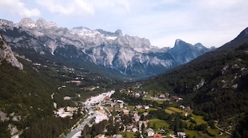 Vista aérea de un valle con montañas altas, cumbres nevadas, río de cauce pedregoso, bosque verde y un pueblo con múltiples casas y un puente.