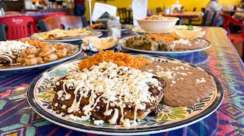 Enchiladas con mole, arroz rojo y frijoles refritos servidos en plato de talavera sobre mantel de hule colorido; fondo de comedor desenfocado.