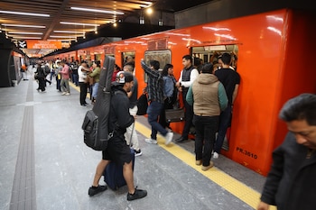 Un tren naranja del Metro CDMX en la estación Auditorio con pasajeros en el andén, entrando y saliendo, y un trabajador de limpieza al fondo