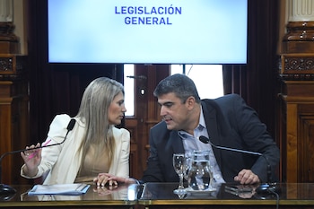 Un hombre y una mujer sentados en una mesa con micrófonos y vasos, conversan bajo una pantalla que muestra 'LEGISLACIÓN GENERAL' en una sala formal