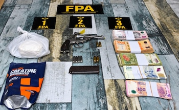 Un arma de fuego, municiones, fajos de billetes de moneda argentina y bolsas con sustancia blanca junto a carteles numerados de la policía FPA