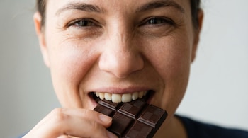 Primer plano del rostro sonriente de una persona mordiendo una barra de chocolate amargo, mostrando la boca, parte de la nariz y los ojos.