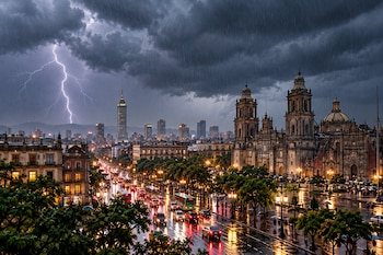 Un rayo ilumina el cielo sobre la Catedral Metropolitana y los rascacielos del centro de la Ciudad de México durante una lluvia intensa.