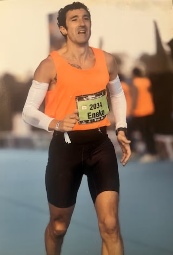 Un corredor masculino con camiseta naranja, pantalones cortos negros y manguitos blancos corre en una competición, con el dorsal 2034 'Eneko'