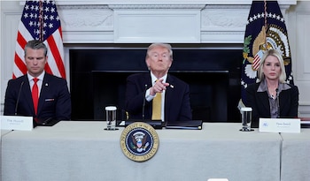 Donald Trump señala al frente, flanqueado por un hombre con corbata roja y una mujer con blusa gris, sentados detrás de una mesa con el sello presidencial