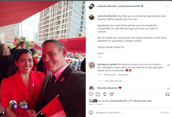Hombre y mujer sonrientes en primer plano con cintas rojas en las solapas. El hombre sostiene una bandera de Perú. Detrás, multitud y edificios