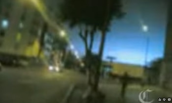 Fotograma borroso de una calle oscura con luces difusas, un árbol central y un cielo oscuro con puntos luminosos. Logotipo de letra C en la esquina inferior derecha