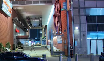 Vista nocturna de una calle de Times Square con cinta policial amarilla. Un oficial de policía se encuentra cerca de un edificio moderno. Un coche oscuro está en primer plano