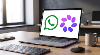 Un computador portátil gris con los logos de WhatsApp y Meta AI en la pantalla, un teclado, un ratón negro y una taza sobre un escritorio de madera.