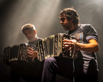 Dos hombres interpretan el bandoneón sobre un escenario iluminado con focos de luz