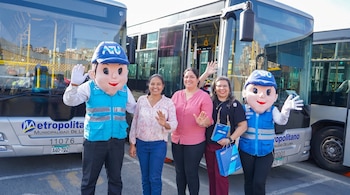 Dos mascotas institucionales de ATU y tres mujeres sonríen frente a dos autobuses del Metropolitano. Una mujer sostiene un cuaderno y una bolsa azul