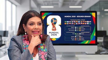 Mujer con blazer gris bordado y aretes llamativos junto a un monitor que muestra el logo del Mundial 2026 y resultados de partidos de fútbol.