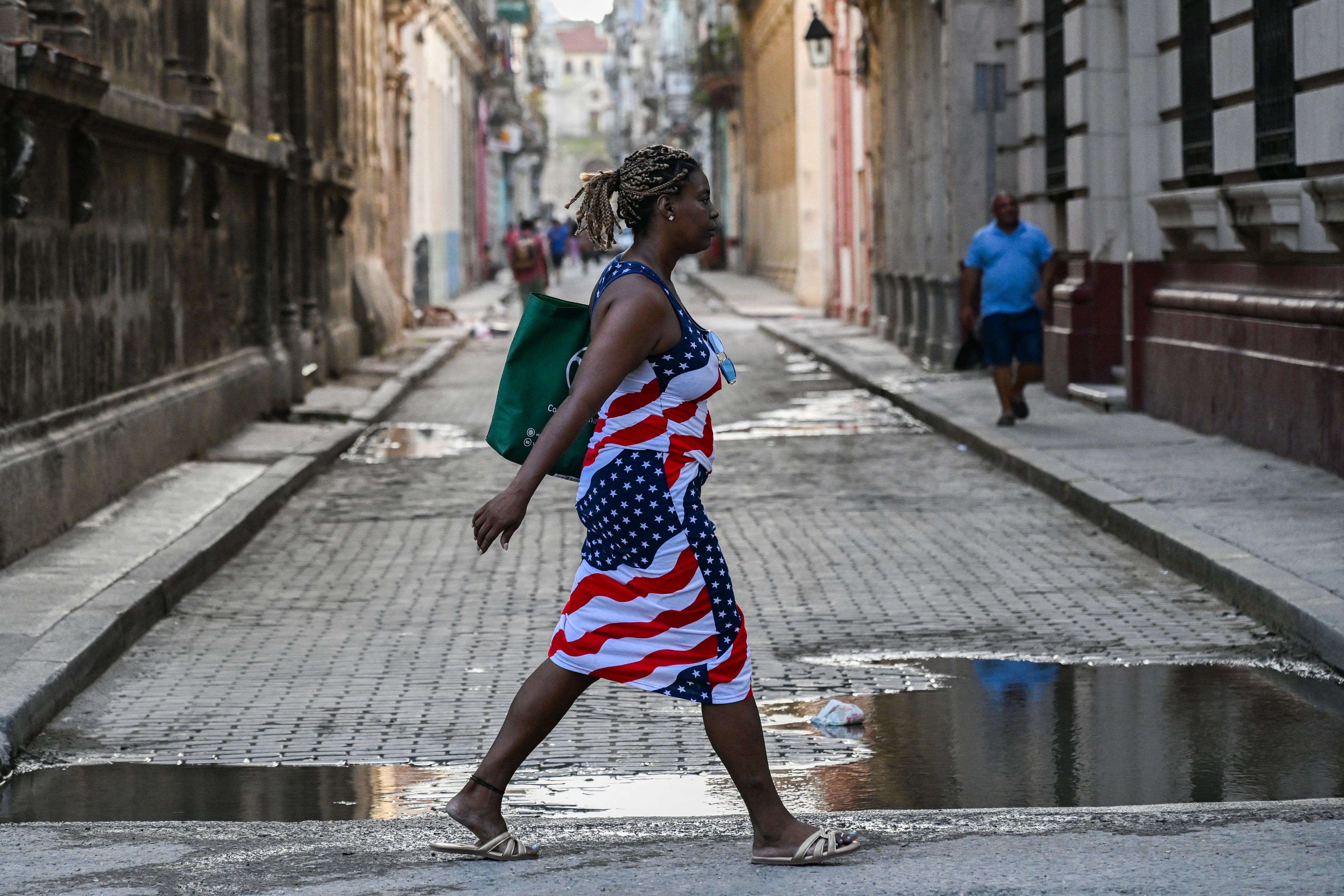 A woman wearing a dress with the US flag crosses a street in Havana on August 18, 2026. Once synonymous with carefree revelry, Havana has been deserted due to power cuts, mass emigration and deep uncertainty about its future. (Photo by YAMIL LAGE / AFP)