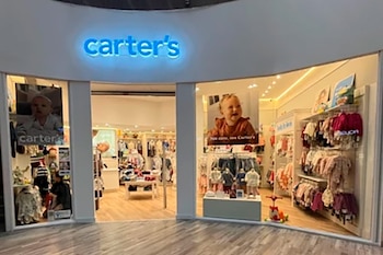 Exterior de un local de ropa infantil Carter's con logotipo azul brillante, escaparates con ropa de bebé y afiches de bebés