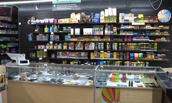Interior de una tienda con estanterías llenas de productos, vitrinas con paquetes y botellas, mostrador y sistema de punto de venta