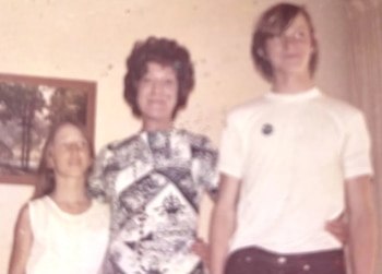 Fotografía antigua de tres personas: una mujer de cabello rizado en el centro, flanqueada por una mujer joven y un hombre joven, posando de pie