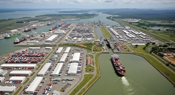 Vista aérea del Canal de Panamá con un barco portacontenedores, esclusas, muelles, grúas, miles de contenedores de carga y almacenes.