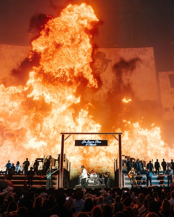 Carín León y su banda tocan en un escenario con grandes llamaradas de fuego de fondo y un letrero que dice De Sonora Para el Mundo