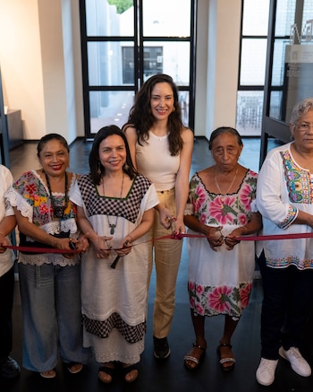 Seis mujeres sonríen mientras cortan una cinta roja con tijeras en una ceremonia. Tres mujeres visten ropa bordada tradicional, otras tres ropa moderna