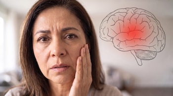 Una mujer sostiene su mejilla con una mano junto a una ilustración de un cerebro humano que tiene una mancha roja luminosa en el centro.
