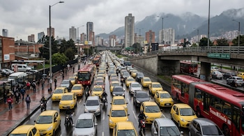 Vista aérea de un trancón con cientos de taxis amarillos y buses rojos TransMilenio en una autopista de Bogotá, con edificios y montañas al fondo bajo un cielo nublado.