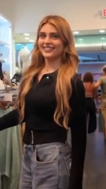 Marta Fort, una mujer joven con cabello rubio ondulado, sonríe ligeramente mientras mira a la izquierda, vestida con un top negro y jeans, en el interior de una tienda de ropa