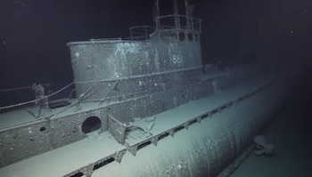 Un submarino hundido en el fondo marino con la estructura metálica cubierta de sedimento y el número 861 impreso