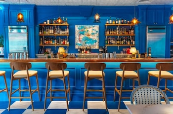 Barra del Bar Please! en Boise, Idaho. Diseño azul vibrante, taburetes de madera, estantes con botellas y suelo a cuadros azul y blanco