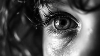 Primer plano de un ojo humano en blanco y negro con la pupila, el iris, las pestañas largas y la piel alrededor del ojo.