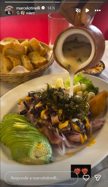 Una mano sirve líquido de una jarra de barro sobre un plato con pescado, cebolla roja, aguacate, maíz, camote, alcaparras y alga